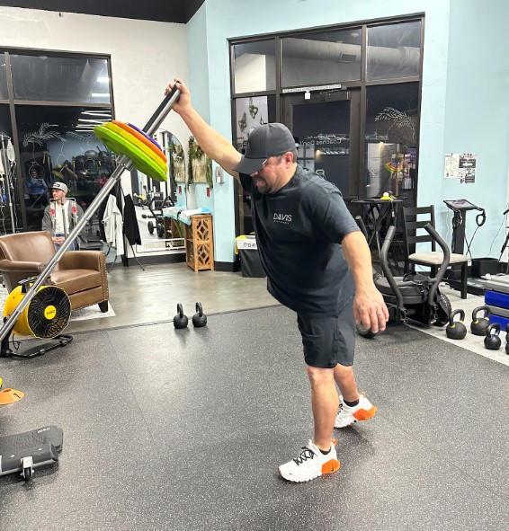 A person performing a controlled one-arm weight exercise, demonstrating the single-side balance and rotational control used in an overhead racquet swing