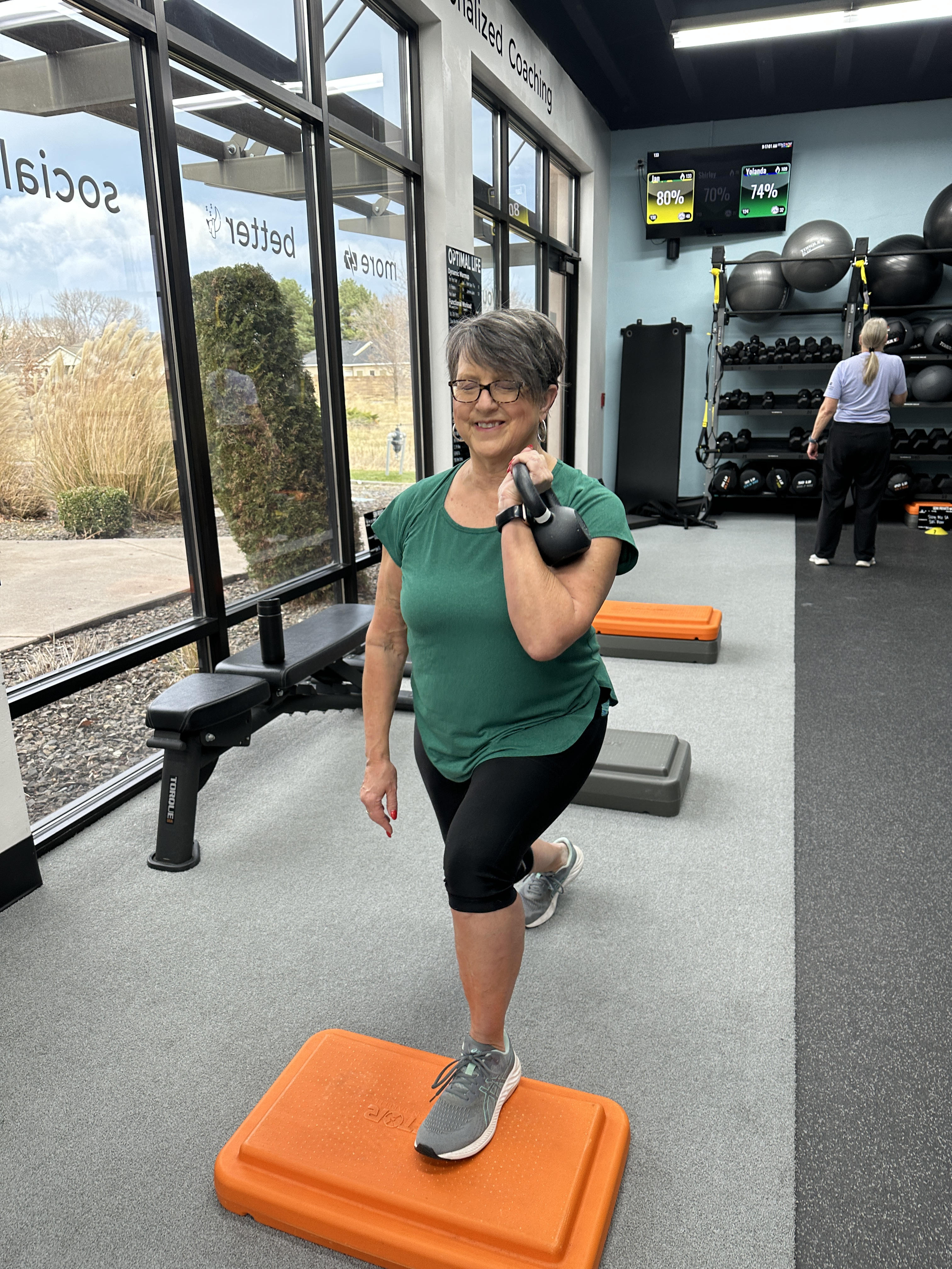 Smiling woman in her 60s lunging with a kettlebell in a modern gym